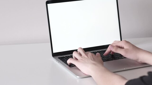 Hands typing on open laptop with blank bright screen in minimalist workspace, showing steady keyboard use on white desk with soft neutral light, clean modern composition for office tasks and online