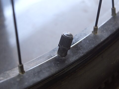 Close-up view of a black plastic valve cap on a bicycle wheel rim, highlighting the tire valve stem mechanism and tread texture