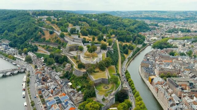 Namur, Belgium. Citadelle de Namur, vast stone fortifications cascading down a forested hillside above the Meuse River, aerial panoramic view on a bright summer day. Drone footage