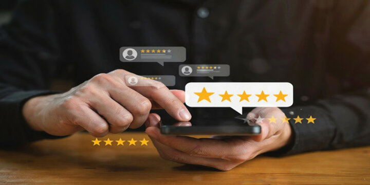 A person uses a smartphone with glowing five-star rating icons emerging from the screen and surrounding it, indicating positive reviews.