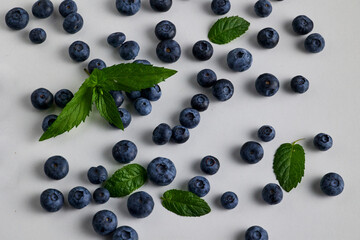 Scattered Fresh Blueberries with Mint Leaves on White Surface © Alex