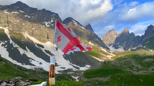 The Georgian flag marks a remote waypoint near Abudelauri Lakes beneath Mount Chaukhi, presenting mountain navigation, trekking safety, route orientation, visitor access, and outdoor tourism