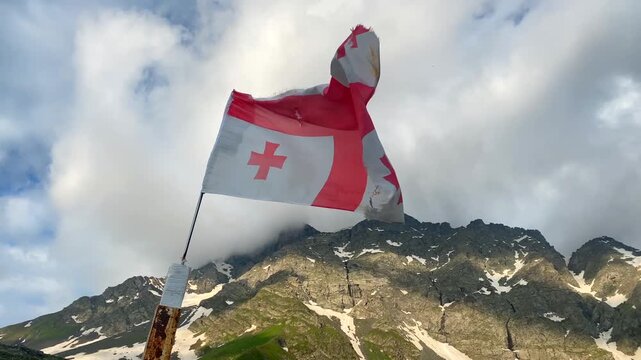 A Georgian flag billows against the snowy Chaukhi range near Abudelauri Lakes, creating a strong destination image for national travel campaigns, mountain tour promotion, cultural outreach