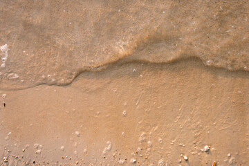 Gentle sea waves washing onto a sandy tropical beach with soft foam, creating a peaceful coastal background ideal for travel, summer, and nature themes. © LulaAlbab