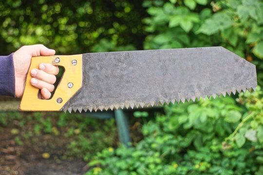 A hand in a glove holds a one metal hacksaw with a yellow handle against a green background in the street