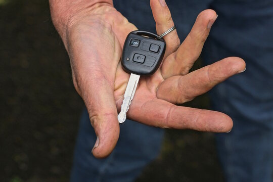 One black gray car key lies on the palm of a hand on a dark background