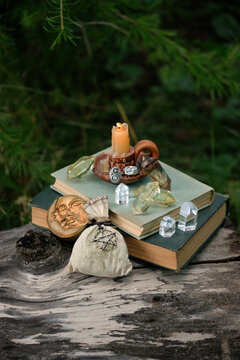 witch items - crystal gemstones, candle, amulets, witch bag, spell books close up on tree trunk in garden or forest. Magic Crystal Ritual, Witchcraft. Esoteric spiritual ceremony. practical magic