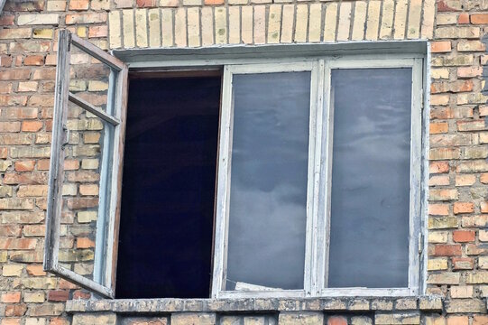 one old white square open wooden window on brown brick wall of house on day street