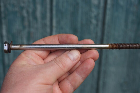 hand holding one old long grey brown iron rusty bolt on green background