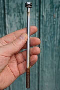 hand holding one old long grey brown iron rusty bolt on green background
