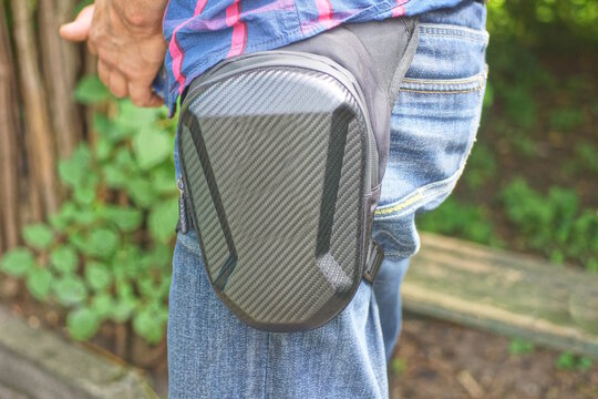 one gray plastic bag, a purse on the waist and leg in blue jeans on the leg on a summer day street
