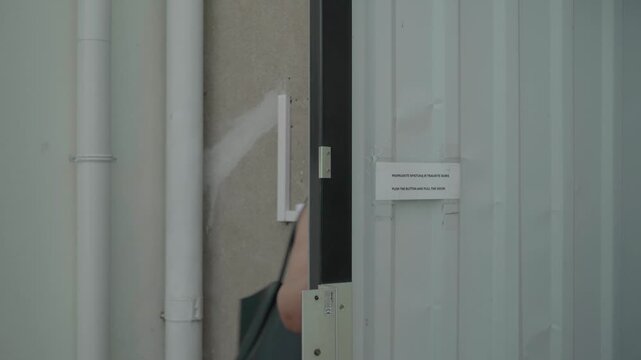 Solo traveler presses an access control button to unlock a metal exit gate and walks through on a hot day.
