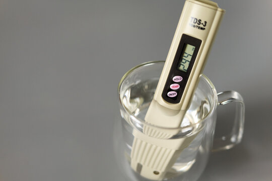 Water quality test with TDS meter in clear glass cup on gray surface