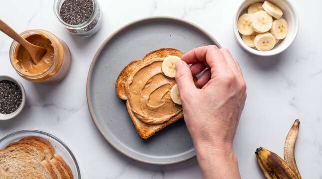 Hand placing banana slices onto peanut butter toast on gray plate