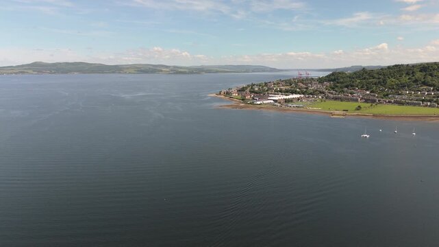 Cinematic aerial drone shot flying towards the coastal town of Greenock, Scotland, featuring the Firth of Clyde and lush green landscapes.