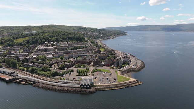 Cinematic aerial orbit showing the scenic coastal town of Gourock, Scotland, featuring the Firth of Clyde, historic architecture, and lush green hills.