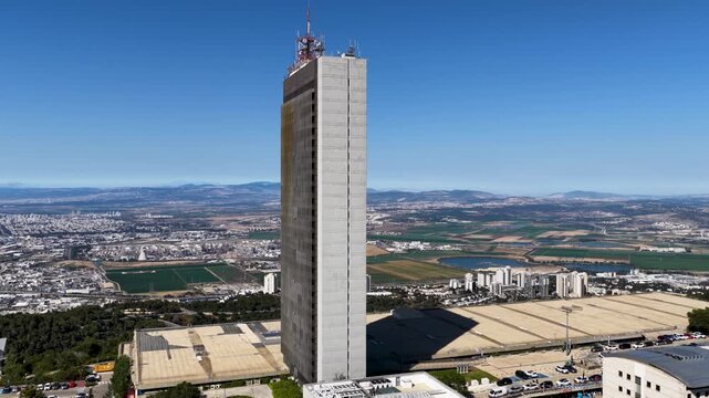 High angle drone shot panning around the brutalist Eshkol Tower building located on the Mount Carmel campus overlooking the landscape below on a clear day