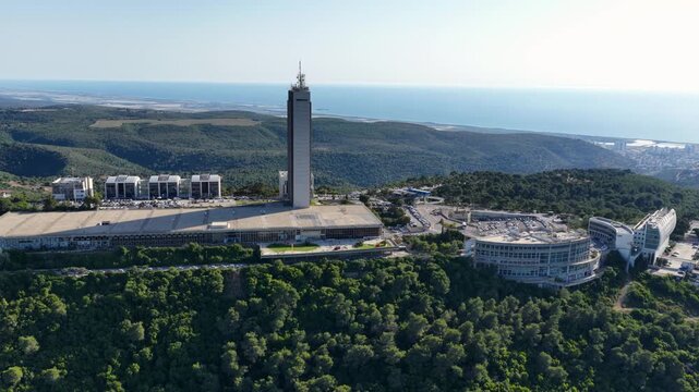 Drone tracking shot showcasing the iconic Eshkol Tower skyscraper and institutional buildings on Mount Carmel ridge overlooking the Mediterranean coast.