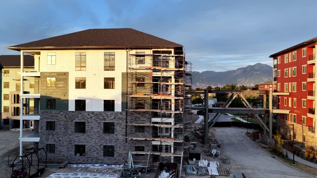 Apartment construction project with residential buildings, active scaffolding, pedestrian skybridge and heavy equipment in Taylorsville, Salt Lake County, Utah, United States, drone forward push in
