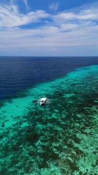 Vertical drone orbits, ascends, and pulls back follow a longboat over reef flats along Dumaluan Beach in Panglao