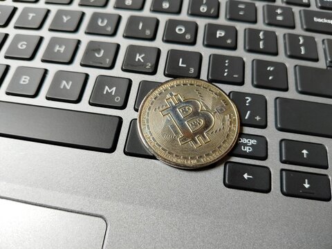 a Bitcoin token resting on a computer keyboard, symbolizing cryptocurrency investment, blockchain security, digital assets, electronic payments, financial markets, and modern fintech concepts.