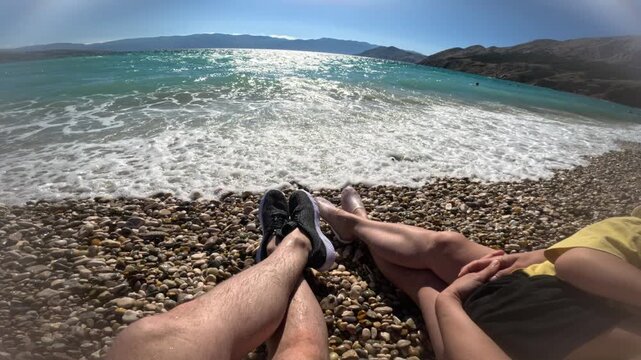family of three relaxing on a pebble beach by blue sea