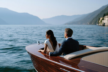 Fototapeta premium A couple enjoys a serene moment on a classic wooden boat, surrounded by the enchanting beauty of a tranquil lake and picturesque mountains in the background.