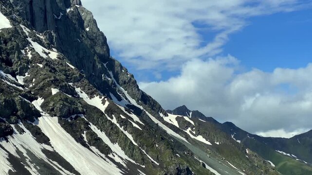 An alpinist climbs above Juta Valley beneath the rocky Chaukhi massif in Georgia, carrying expedition gear across steep terrain and linking mountain tourism with human endurance