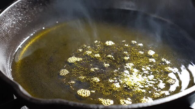 Green olive oil bubbling and steaming in hot cast iron skillet in macro view
