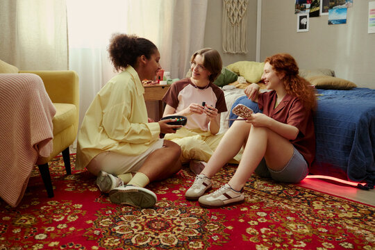 Young girls sitting on floor, chatting and sharing cosmetics during sleepover, expressing friendship and social bonding. Ideal for youth lifestyle, beauty, community campaigns