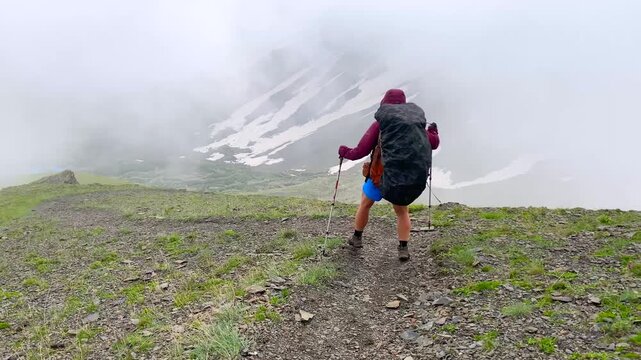 A backpacker advances through dense fog across the rocky Chaukhi Pass, using trekking poles for stability while the harsh alpine weather conveys preparedness, endurance, navigation, and expedition