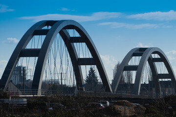 Fototapeta premium Modern steel arch bridge with suspension cables over an urban construction area