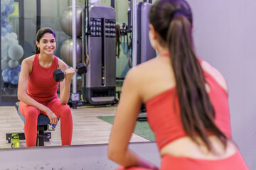 Fototapeta premium Woman lifts dumbbells while smiling in a gym mirror