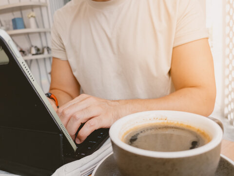 Focused man typing on a modern tablet device, accompanied by a warm cup of coffee