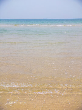Clear turquoise ocean water gently washes golden sand under a bright summer sky.