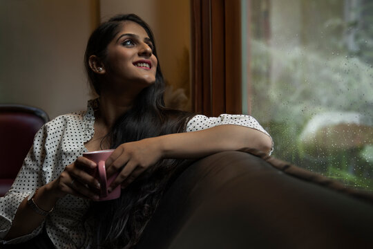 PORTRAIT OF A YOUNG WOMAN HAPPILY LOOKING OUTSIDE OFFICE ROOM ON A RAINY DAY