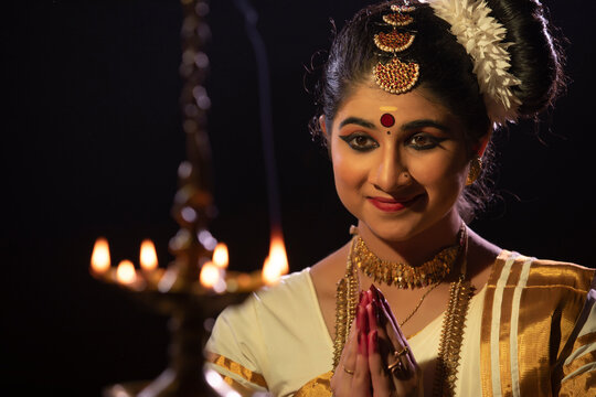 Mohiniattam dancer praying with her hands joined in front of a lamp