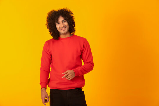 A CURLY HAIRED MAN CASUALLY POSING IN FRONT OF CAMERA