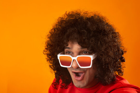 A CURLY HAIRED YOUNG MAN WEARING GOGGLES LOOKING AWAY SURPRISED