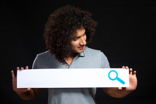 A CURLY HAIRED YOUNG MAN HOLDING SEARCH BAR AND LOOKING AT IT