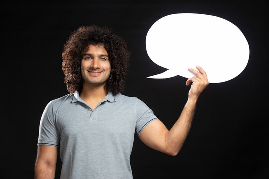 A CURLY HAIRED YOUNG MAN HOLDING THOUGHT BUBBLE AND SMILING AT CAMERA