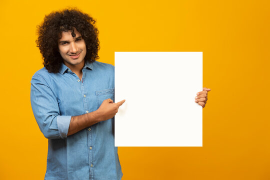 A YOUNG MAN WITH CURLY HAIR HOLDING A LARGE SHEET OF PAPER AND POINTING AT IT