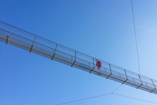 Hiker crossing suspension footbridge against clear sky