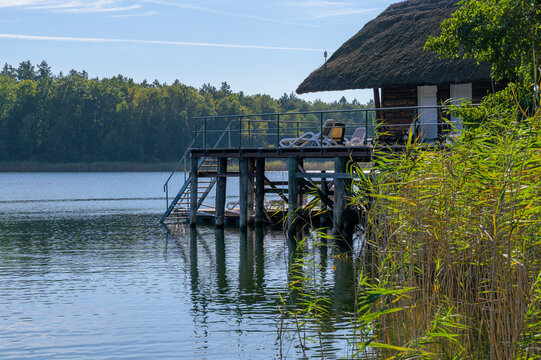 Wooden pier with thatched roof cottage on a quiet lake. Wooden jetty and a rustic hut with a thatched roof built over the calm water of D&ouml;llnsee lake, Schorfheide Germany.