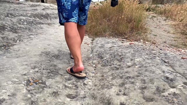 A tourist in sandals walks across weathered rock paths at Uplistsikhe, highlighting visitor mobility, archaeological terrain, cultural tourism and practical access through Georgia's ancient settlement