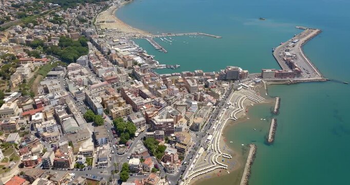 Panorama of Anzio, a city in province of Rome, Lazio, Italy. Aerial view of a sunny coastal town featuring a bustling harbor, long pier, turquoise sea waters, sandy beaches with umbrellas. 