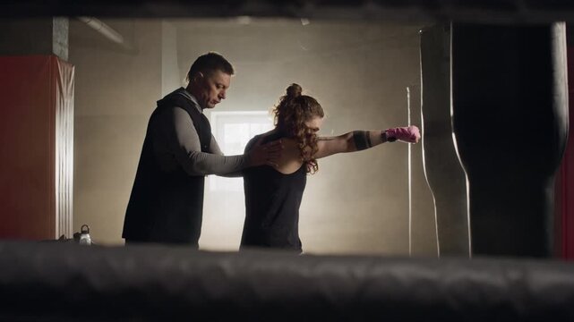 Middle aged Caucasian male coach correcting stance and punch technique of young Caucasian female boxer in gym. Video suitable for fitness brands and sports coaching advertisements