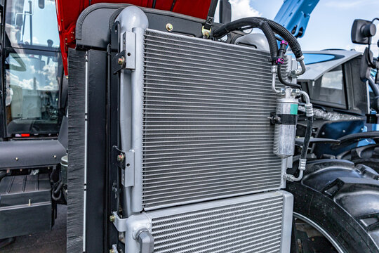 Agricultural tractor engine cooling radiators package. Modern farm machinery cooling system section with a c condenser, oil intercooler, receiver drier and industrial transport vehicle details.