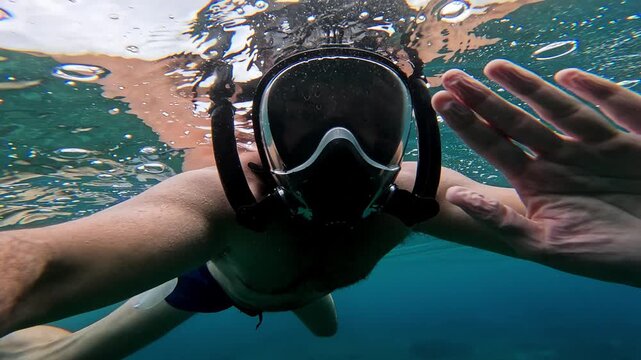 First person view of a snorkeler diving underwater with a full face mask in the clear turquoise ocean