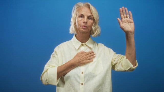 Woman with right hand raised and left hand on chest in studio performing oath gesture; solemn pledge.